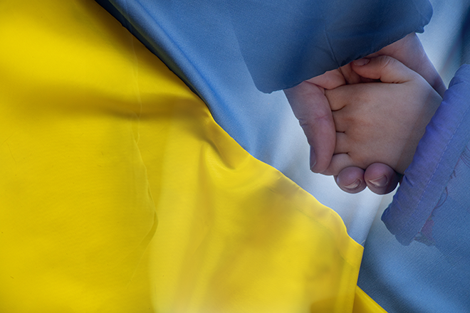 Mother holds a little girl by the hand against the background of the national flag of Ukraine yellow-blue. Peace in Ukraine, stop the war.